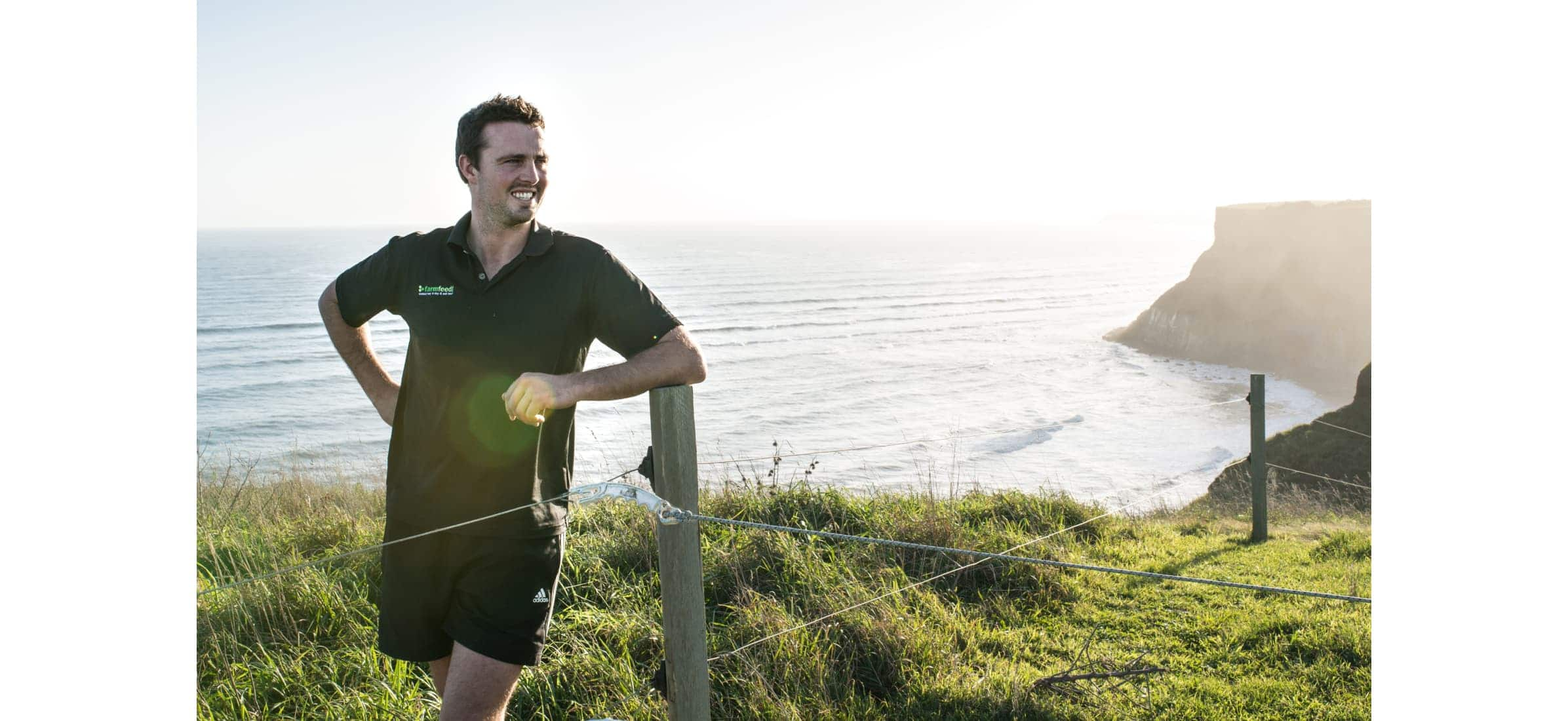 Simon stands chuffed as he leans on a fence, looking over the ocean from up on a hill.